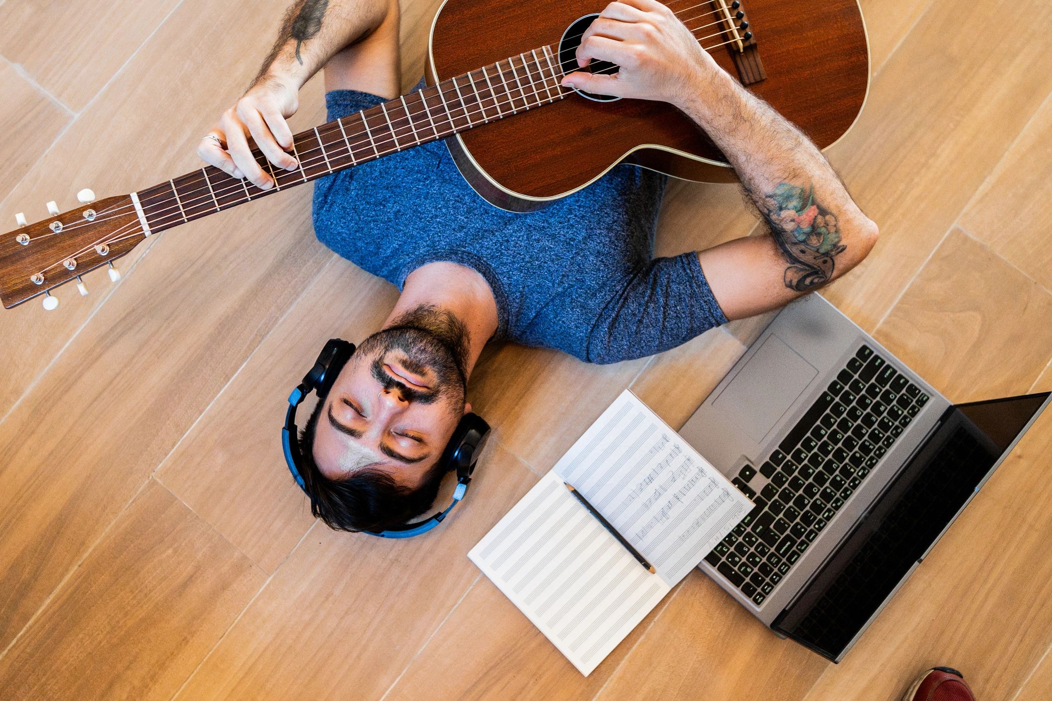 Mid adult man listening music and playing guitar lying down on floor